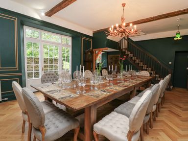 A dining room with a large wooden table set with glasses candlesticks and flowers surrounded by upholstered chairs at Llwynderw Hall in Abergwesyn near Llanwrtyd Wells