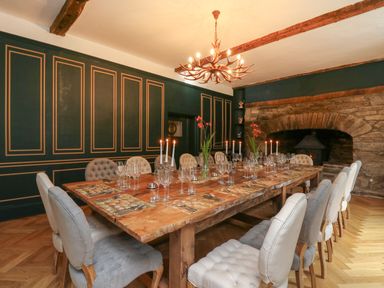 A dining room with a large wooden table set with glasses candles and flowers surrounded by upholstered chairs and a stone fireplace at Llwynderw Hall in Abergwesyn near Llanwrtyd Wells