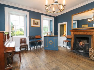 A room with a piano wooden floor bar stools fireplace and large mirror at Llwynderw Hall in Abergwesyn near Llanwrtyd Wells