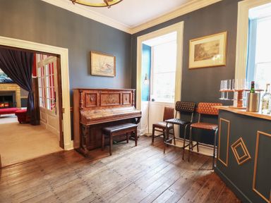 A room with a wooden piano a bench three chairs two framed pictures and a bar with glasses at Llwynderw Hall in Abergwesyn near Llanwrtyd Wells