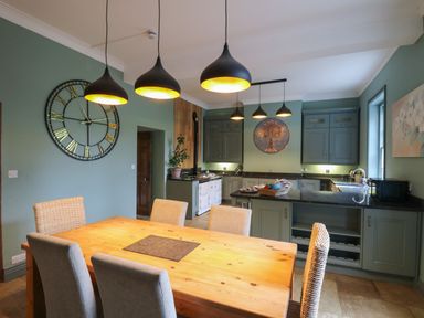 A kitchen with green cabinets a wooden dining table and hanging black pendant lights at Llwynderw Hall Abergwesyn near Llanwrtyd Wells