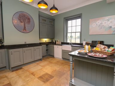 A kitchen with grey cabinets black countertops a window and a small island with food and drinks at Llwynderw Hall in Abergwesyn near Llanwrtyd Wells