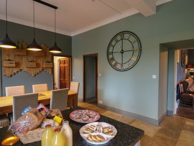 A dining area with a wooden table and chairs a large wall clock and food on a kitchen counter at Llwynderw Hall in Abergwesyn near Llanwrtyd Wells
