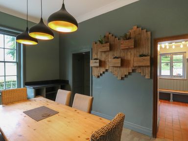 A dining room with a wooden table and chairs hanging pendant lights and wall planters at Llwynderw Hall in Abergwesyn near Llanwrtyd Wells