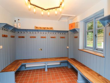 A changing room with wooden benches and labeled hooks and windows showing an outdoor view at Llwynderw Hall in Abergwesyn near Llanwrtyd Wells