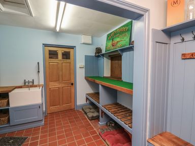 A utility room with a wooden door a sink shelves with baskets and pet beds on a tiled floor at Llwynderw Hall in Abergwesyn near Llanwrtyd Wells