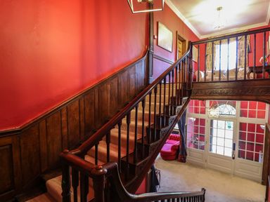 A staircase with wooden banisters and red walls overlooking a sitting area with a sofa and a door with glass panels at Llwynderw Hall in Abergwesyn near Llanwrtyd Wells