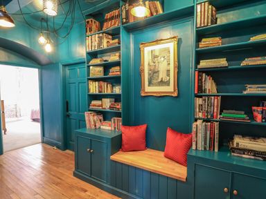 A room with built in blue bookshelves filled with books wooden bench with red cushions and framed picture on wall