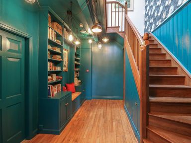 A hallway with teal walls wooden stairs and built in bookshelves with books and cushions at Llwynderw Hall in Abergwesyn near Llanwrtyd Wells