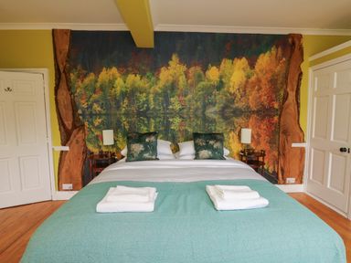 A bedroom with a bed covered by a blue blanket and white towels on top with two green pillows and a wall mural of autumn trees at Llwynderw Hall in Abergwesyn near Llanwrtyd Wells