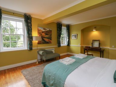 A bedroom with a bed and folded towels a green chair a floor lamp windows with curtains and a dresser at Llwynderw Hall in Abergwesyn near Llanwrtyd Wells