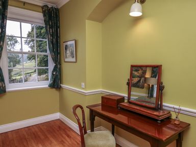 A room with a wooden table and mirror beside a window with curtains at Llwynderw Hall in Abergwesyn near Llanwrtyd Wells