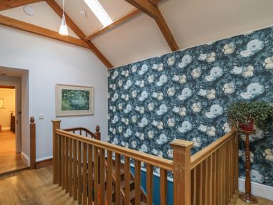 An upstairs hallway with wooden banisters floral wallpaper plant on a wooden stand and a framed picture at Llwynderw Hall in Abergwesyn near Llanwrtyd Wells