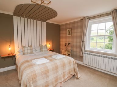 A bedroom with a double bed covered in plaid blankets and pillows beside a window at Llwynderw Hall in Abergwesyn near Llanwrtyd Wells
