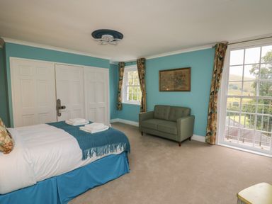 A bedroom with a bed and blue bedspread green loveseat and large windows at Llwynderw Hall in Abergwesyn near Llanwrtyd Wells