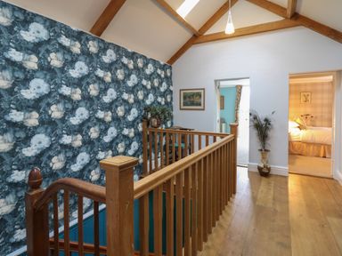 A hallway with wooden railings overlooking a staircase floral wallpaper and two adjoining rooms at Llwynderw Hall Abergwesyn near Llanwrtyd Wells