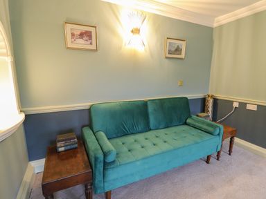 A teal sofa between two wooden side tables with books and a decorative vase on a carpeted floor at Llwynderw Hall in Abergwesyn near Llanwrtyd Wells