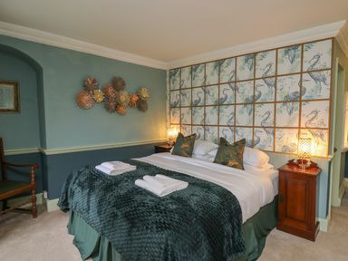 A bedroom with a double bed bedside tables lamps a wooden chair and decorative wall panels at Llwynderw Hall in Abergwesyn near Llanwrtyd Wells