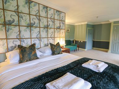 A bedroom with a large bed towels on a blanket a green sofa and bird wallpaper at Llwynderw Hall in Abergwesyn near Llanwrtyd Wells