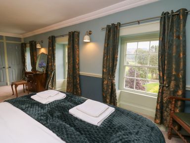 A bedroom with a bed with towels on the blanket a vanity with a mirror and flowers and windows with curtains at Llwynderw Hall in Abergwesyn near Llanwrtyd Wells