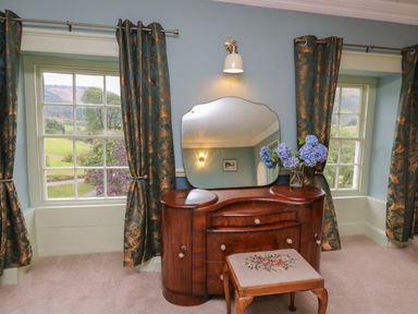A dressing table with a mirror and a stool between two windows with curtains at Llwynderw Hall in Abergwesyn near Llanwrtyd Wells