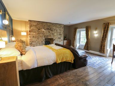 A bedroom with a bed a stone fireplace wooden floor and windows with curtains at Llwynderw Hall in Abergwesyn near Llanwrtyd Wells