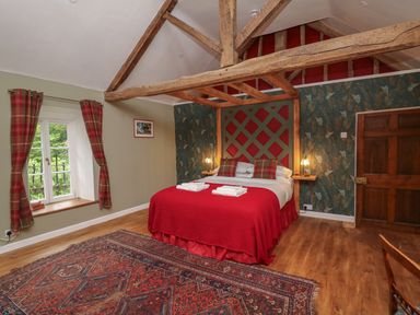 A bedroom with a bed with red bedding and plaid pillows wooden beams on the ceiling a window with plaid curtains and a patterned rug on the floor at Llwynderw Hall in Abergwesyn near Llanwrtyd Wells