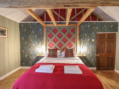 A bedroom with a double bed red blanket plaid pillows and wooden beams on the ceiling at Llwynderw Hall in Abergwesyn near Llanwrtyd Wells