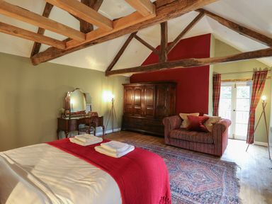 A bedroom with a bed with red blanket two folded towels a wooden dressing table an armchair a large rug and wooden beams on the ceiling at Llwynderw Hall in Abergwesyn near Llanwrtyd Wells