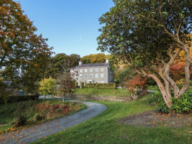 A gravel driveway leading to a three-story stone house surrounded by trees and grass at Llwynderw Hall in Abergwesyn near Llanwrtyd Wells