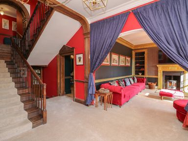 A living room with red walls wooden staircase red sofa and fireplace at Llwynderw Hall in Abergwesyn near Llanwrtyd Wells