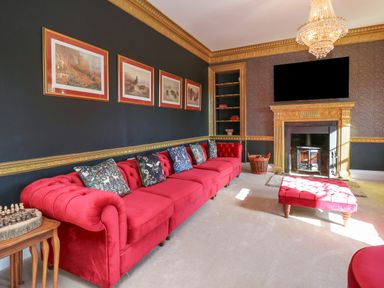 A sitting room with a red sofa red ottoman fireplace and paintings on the wall at Llwynderw Hall in Abergwesyn near Llanwrtyd Wells