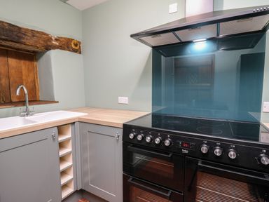 A kitchen corner with a sink faucet wine rack cabinets oven and stove at Llwynderw Hall in Abergwesyn near Llanwrtyd Wells
