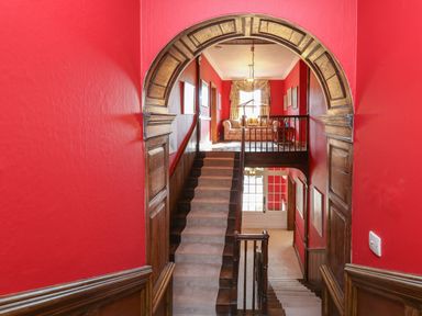A stairway with wooden arch and red walls leading to a sitting area with sofa and window at Llwynderw Hall in Abergwesyn near Llanwrtyd Wells