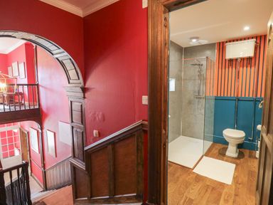 A bathroom with a shower and toilet next to a wooden staircase with red walls at Llwynderw Hall in Abergwesyn near Llanwrtyd Wells