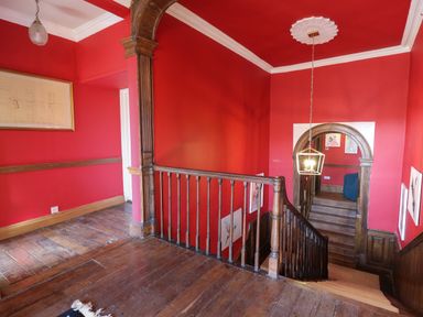 A stairway with wooden banisters and red walls with framed artwork at Llwynderw Hall in Abergwesyn near Llanwrtyd Wells