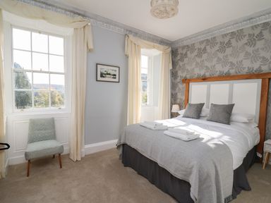 A bedroom with a double bed gray pillows and a chair by the window at Llwynderw Hall in Abergwesyn near Llanwrtyd Wells