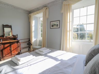 A bedroom with a bed next to windows and a wooden dresser with a mirror at Llwynderw Hall in Abergwesyn near Llanwrtyd Wells