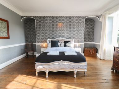 A bedroom with a bed and black pillows a wooden chest a rocking chair and a wooden dresser at Llwynderw Hall in Abergwesyn near Llanwrtyd Wells