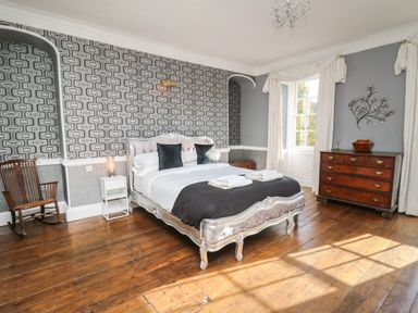 A bedroom with a bed wooden rocking chair wooden chest of drawers and patterned wallpaper at Llwynderw Hall in Abergwesyn near Llanwrtyd Wells