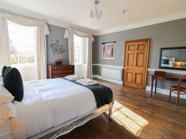 A bedroom with a bed a wooden chest of drawers a wooden desk a chair and windows with curtains at Llwynderw Hall in Abergwesyn near Llanwrtyd Wells