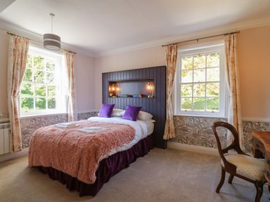 A bedroom with a double bed between two windows and a wooden chair at Llwynderw Hall in Abergwesyn near Llanwrtyd Wells