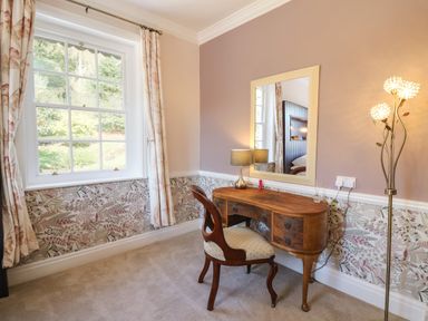 A room with a wooden desk, a chair, a mirror, a table lamp, and a floor lamp at Llwynderw Hall in Abergwesyn near Llanwrtyd Wells