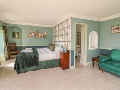 A bedroom with a double bed a wooden chair a green sofa and an open door to a bathroom at Llwynderw Hall in Abergwesyn near Llanwrtyd Wells