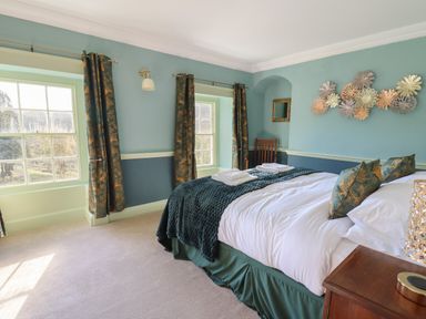 A bedroom with a large bed with pillows and folded towels near two windows with curtains at Llwynderw Hall in Abergwesyn near Llanwrtyd Wells