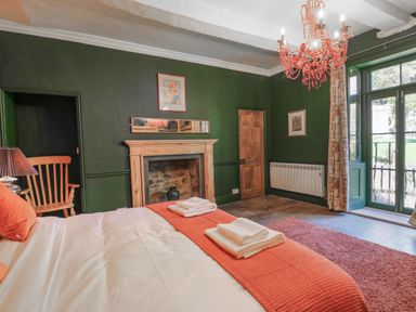 A bedroom with a bed with orange bedding a fireplace wooden chair and glass doors at Llwynderw Hall in Abergwesyn near Llanwrtyd Wells