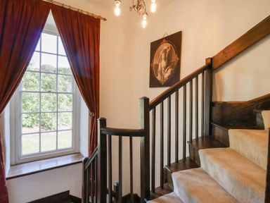 A stairway with beige carpet and wooden railings next to a window with red curtains and a framed portrait on the wall at Llwynderw Hall in Abergwesyn near Llanwrtyd Wells