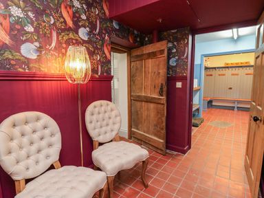 A hallway with two upholstered chairs a floor lamp and an open wooden door leading to a locker room at Llwynderw Hall in Abergwesyn near Llanwrtyd Wells