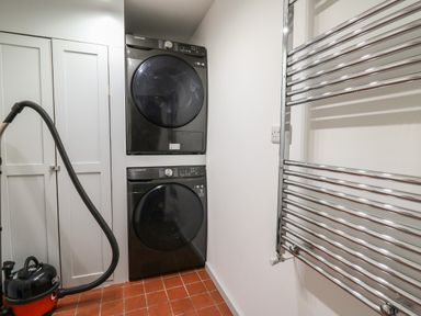 A laundry room with a stacked washer and dryer a vacuum cleaner a towel radiator and a cabinet at Llwynderw Hall in Abergwesyn near Llanwrtyd Wells