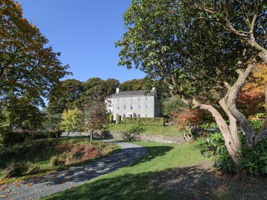 A gravel driveway leading to a three-story stone house surrounded by trees at Llwynderw Hall in Abergwesyn near Llanwrtyd Wells